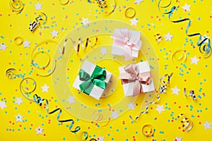 Gift or present box decorated colorful confetti, star, candy and streamer on yellow table top view. Flat lay style. Birthday.