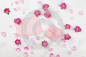 Gift or present box, envelope, paper blank, petals and pink rose flower on white table top view in flat lay style. Greeting card