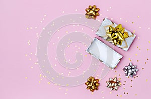 Gift or present box with a gold bow and star confetti on a pink table. Flat lay winter festive background.