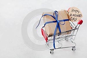 Gift or present box and notes Happy Fathers Day in shopping cart on light background