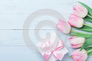 Gift or present box and pink tulip flowers on blue wooden table top view. Greeting card for Womans or Mothers Day. Flat lay.