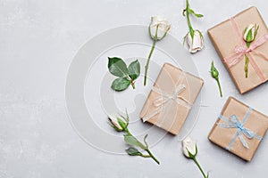 Gift or present box wrapped in kraft paper and rose flower on gray table from above. Flat lay styling. Copy space for text.