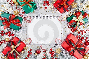 Gift or present boxes, empty notebook, snowy fir tree and christmas decorations on white wooden table top view. Flat lay. Planning