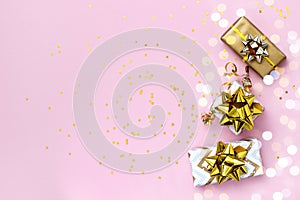 Gift or present boxes with gold bows, Christmas balls and confetti on a pink background, top view. Christmas and New Year card