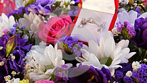 Gift present red box with a set of engagement ring and earrings on the background of a multi-colored beautiful bouquet