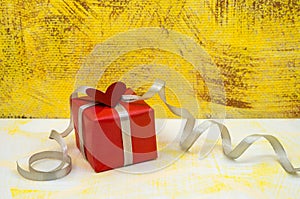 Gift in red packaging with silver-gray ribbon, valentine`s day accessory, gray-yellow background, birthday gift, valentine`s day