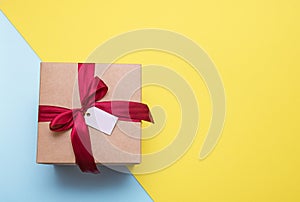 gift with red satin ribbon and blank tag on yellow and blue background, copy space