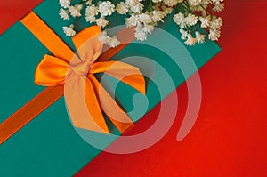 Gift with ribbon and white flowers lie on red background top view copy space