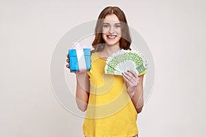 Gift shopping. Happy teenager girl in yellow T-shirt holding present box and euro money banknotes