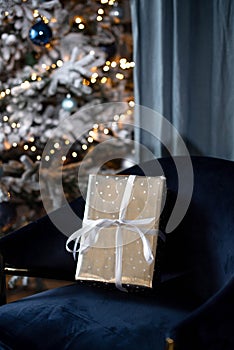 A gift in a silver wrapper with a white ribbon on a velvet blue chair