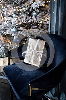A gift in a silver wrapper with a white ribbon on a velvet blue chair