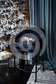 A gift in a silver wrapper with a white ribbon on a velvet blue chair