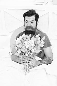 Gift for spouse. Bearded hipster in bed. Spring in bedroom. Man hold tulips bouquet while relaxing in bed. Tender bloom