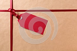 Gift tag and red ribbon, brown parcel wrapping paper background, copy space