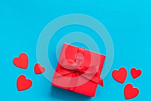 Gift to a sweetheart on Valentine`s Day. Red present box near hearts on blue background top-down copy space