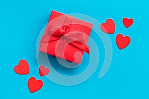 Gift to a sweetheart on Valentine`s Day. Red present box near hearts on blue background top-down copy space