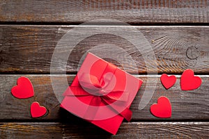 Gift to a sweetheart on Valentine`s Day. Red present box near hearts on dark wooden background top-down copy space