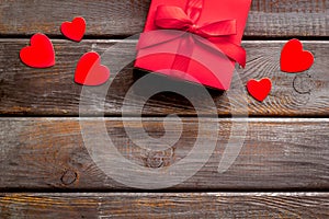 Gift to a sweetheart on Valentine`s Day. Red present box near hearts on dark wooden background top-down copy space