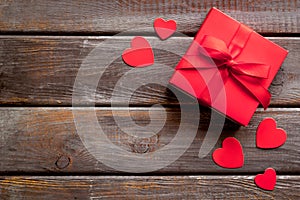 Gift to a sweetheart on Valentine`s Day. Red present box near hearts on dark wooden background top-down copy space