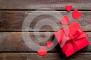 Gift to a sweetheart on Valentine`s Day. Red present box near hearts on dark wooden background top-down copy space