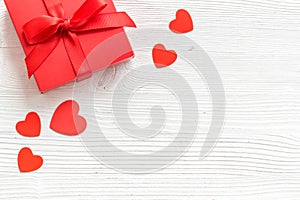 Gift to a sweetheart on Valentine`s Day. Red present box near hearts on white wooden background top-down copy space