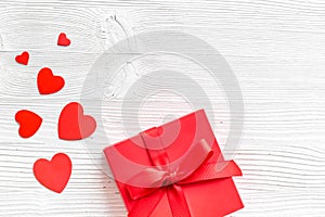 Gift to a sweetheart on Valentine`s Day. Red present box near hearts on white wooden background top-down copy space