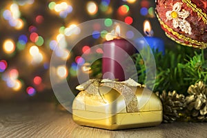 Gift with two candles and Christmas toy with multi-colored lights on background