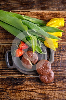 A gift for Valentine`s Day. Romantic treat. Strawberries, chocolate cookies and yellow tulips on a wooden background. Top view.