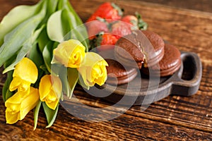 A gift for Valentine`s Day. Romantic treat. Yellow tulips, biscuits and strawberries on a wooden table. A nice gift for your belo