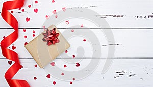 Gift on a white wooden background with a red bow, scattered red hearts, satin ribbon. Valentine`s day. Top view, free space for