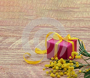 A gift on a wooden background. Gift and yellow mimosa close-up