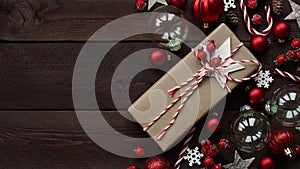 Gift wrapped in craft brown paper lies among holiday decor, red balls, stars, snowflakes and berries on wooden background, copy