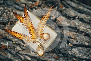 A gift wrapped in craft paper and decorated with dried fern leaves and glass acorns.