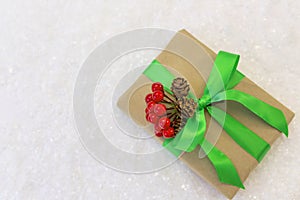 Gift wrapped in craft paper and decorated with green and red ribbons flat lay with snow on background