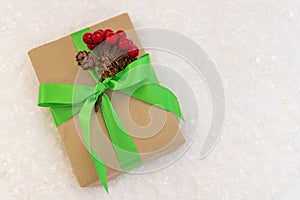 Gift wrapped in craft paper and decorated with green ribbon flat lay with snow on background