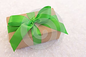Gift wrapped in craft paper and decorated with green ribbon flat lay with snow on background
