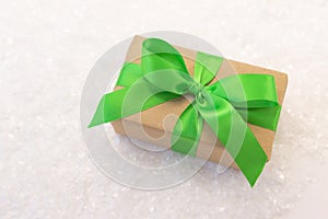 Gift wrapped in craft paper and decorated with green ribbon flat lay with snow on background