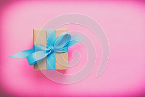 Gift wrapped and decorated with blue bow on pink background with copy space. Flat lay, top view