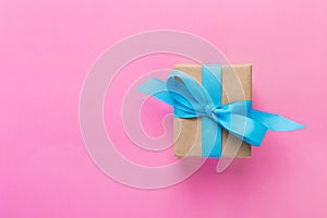 Gift wrapped and decorated with blue bow on pink background with copy space. Flat lay, top view