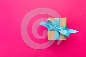 Gift wrapped and decorated with blue bow on pink background with copy space. Flat lay, top view