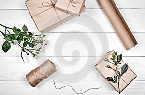 Gift wrapping background, copy space. Rolls of kraft wrapping paper, twine, branch of roses, gift boxes on wooden background