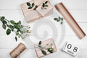 Gift wrapping background, copy space. Rolls of kraft wrapping paper, twine, branch of roses, gift boxes on wooden background.