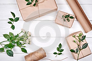 Gift wrapping background. Rolls of kraft wrapping paper, twine, branch of roses, gift boxes on wooden background, copy space.