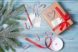 Gift wrapping, gift box with tags, ribbon, candy canes and snow fir tree branch, wooden background, top view
