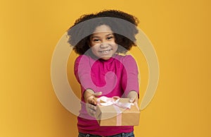 Gift For You. Adorable Black Girl Giving Present Box At Camera photo