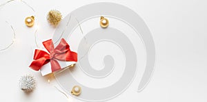 Gifts background. White gift box with red ribbon, New Year balls and sparkling lights garland in Christmas composition