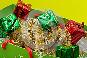 Gifts in a colorful paper bag decorated with Tinsel Garlands on bright yellow background. Christmas gift decoration. New Year