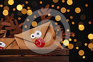 Gifts in envelopes with deer faces in wooden crate against blurred lights, closeup. Christmas advent calendar