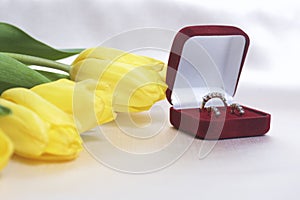 Gifts for loved ones. A bouquet of yellow tulips is scattered on a light surface. Nearby is an open velvet box of red color with g