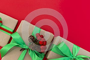 Gifts wrapped in craft paper and decorated with green and red ribbons flat lay on red background